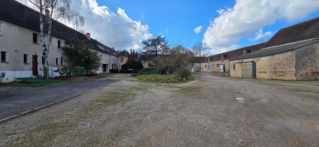 Vue d'une cour spacieuse avec des bâtiments traditionnels en pierre, entourée d'arbres et d'un ciel nuageux.